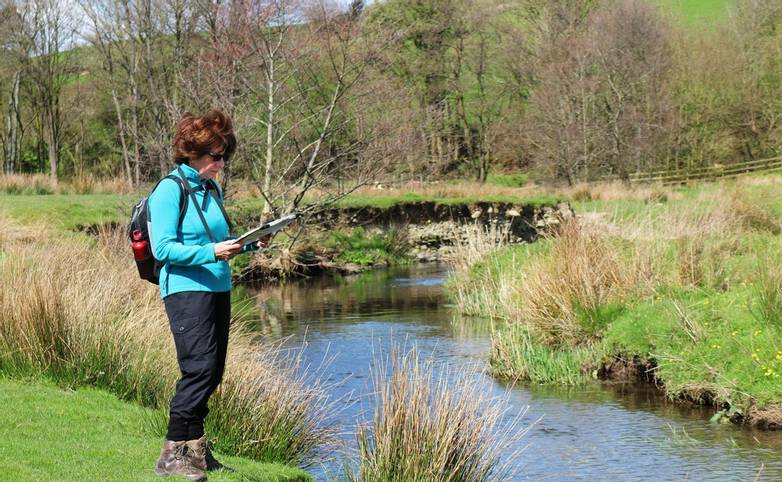 Lady Rambler standing by a river in the Yorkshire Dales reading a map