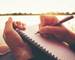 Close up hand of young woman with pen writing on notebook at riverside in the evening.