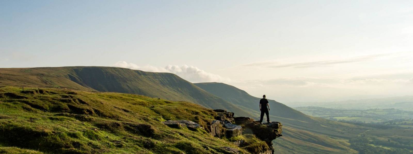 A man standing on the edge of a mountain, looking out across an escarpment, Black Mountains, Brecon Beacons, UK.