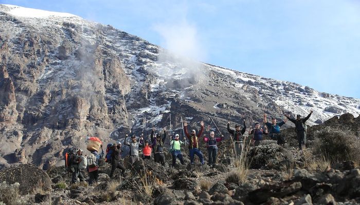 A group of hikers walking over a rocky outcrop surrounded by mountains on the way to Kilimanjaro