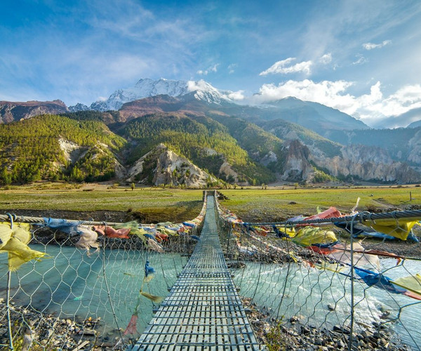 A long suspension bridge covered in colourful prayer flags reaching off into the distant Annapurna Massif