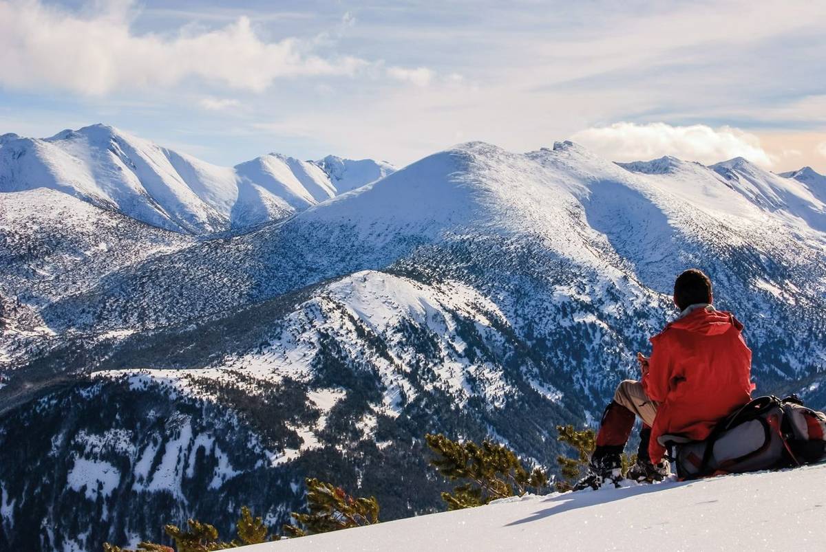 A man is resting , sitting on his backpack. Staring at the snow mountain.