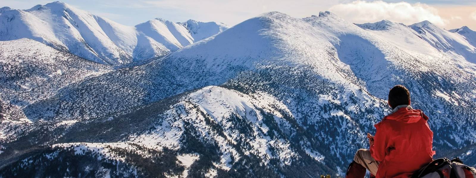 A man is resting , sitting on his backpack. Staring at the snow mountain.