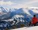 A man is resting , sitting on his backpack. Staring at the snow mountain.