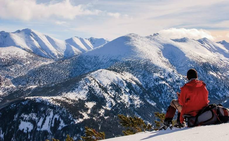 A man is resting , sitting on his backpack. Staring at the snow mountain.