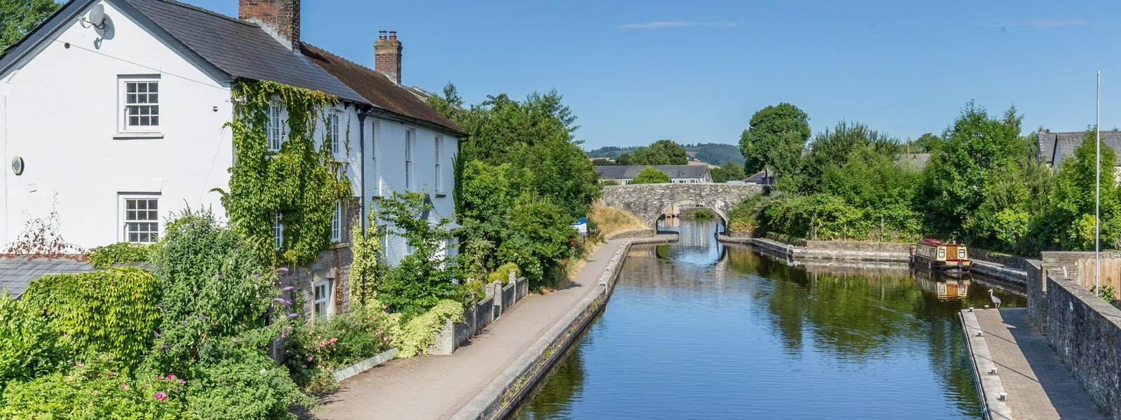 Cottages, bridge and barge reflecting in the water of Brecon Canal basin in Brecon town, Brecon Beacons National Park, Wa…