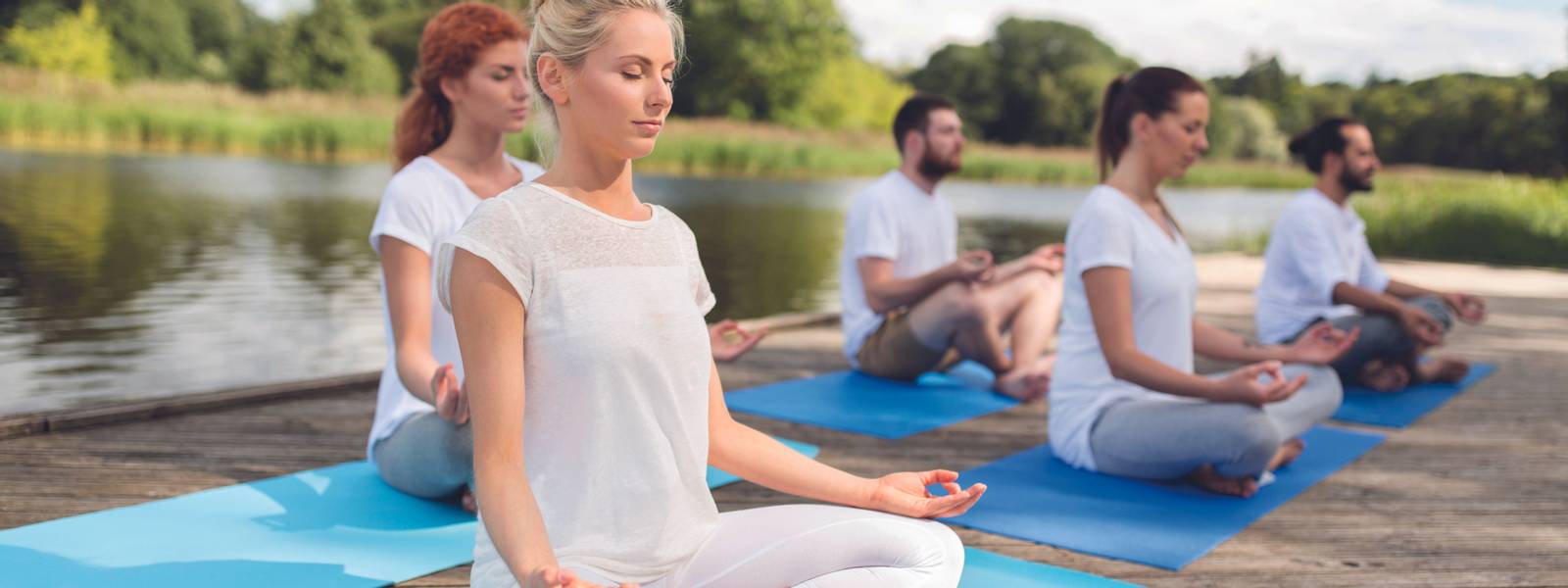 fitness, sport, yoga and healthy lifestyle concept - group of people meditating in lotus pose on river or lake berth