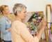 creativity, education and people concept - senior woman with brush and palette painting still life picture on easel at art s…