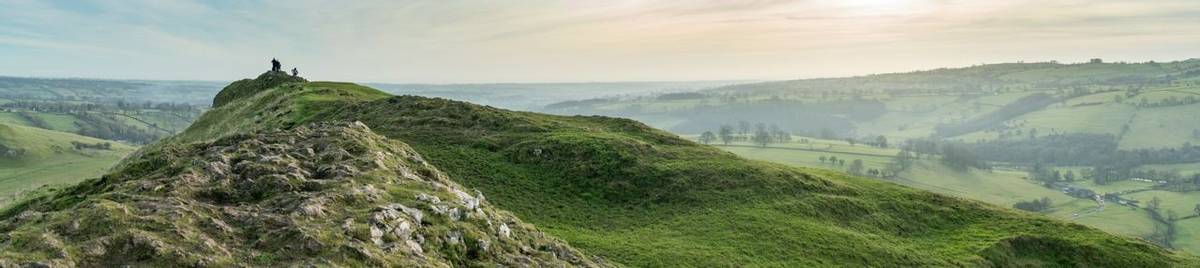 Panoramic view of the summit of Thorpe Cloud with hikers enjoying scenery, Peak District, Derbyshire.