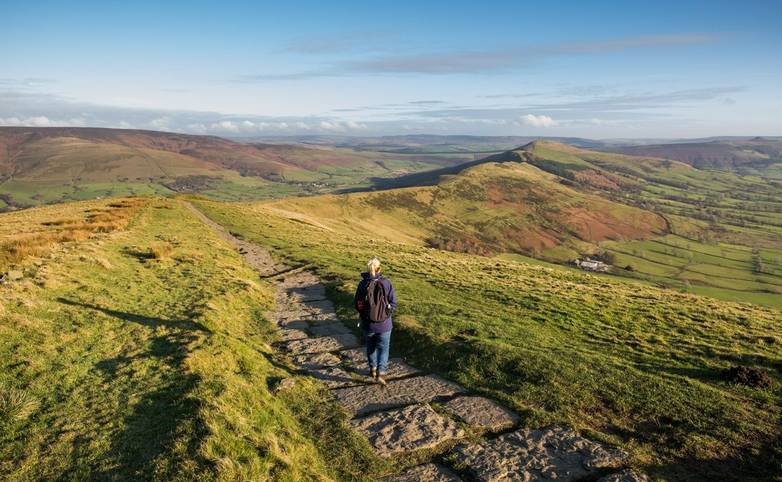 Woman walking the stone path from Mam Tor to Hollins Cross near Castleton in the Peak District, Derbyshire, UK.