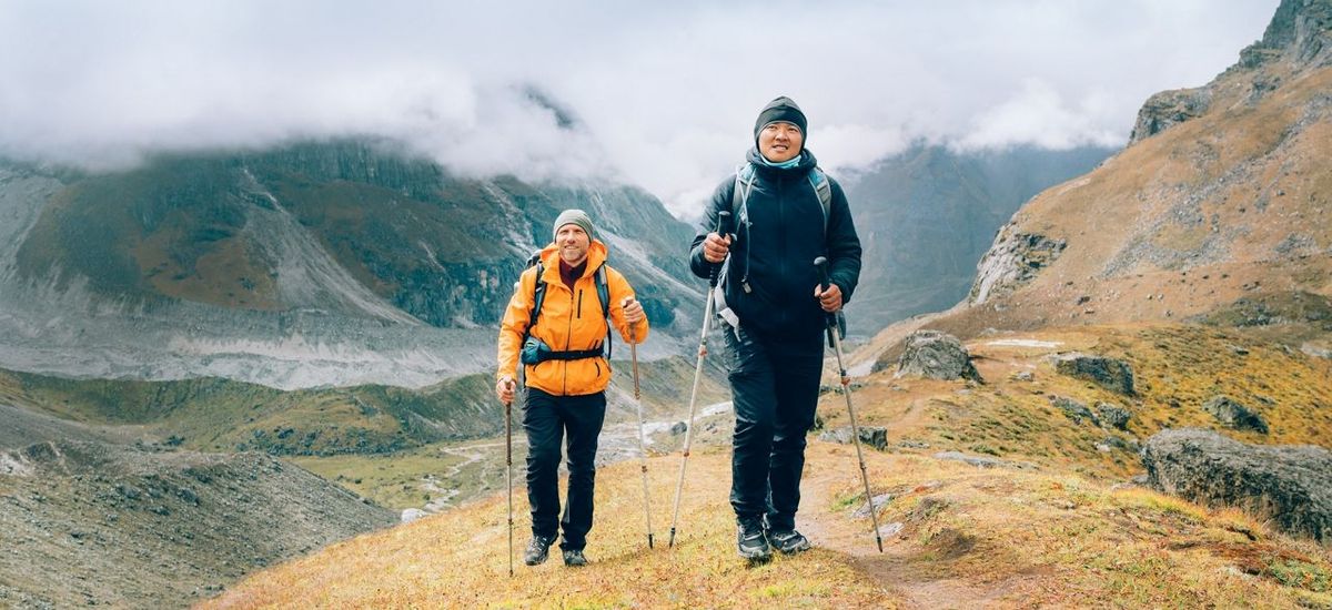 Caucasian and Asian men with backpacks together following Makalu Barun Park trekking route near Khare. Mera peak climbing ac…