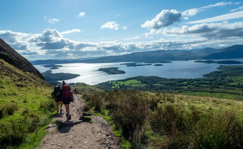 two girls hiking with beautiful lake (loch lomond) and green landscape on a sunny day