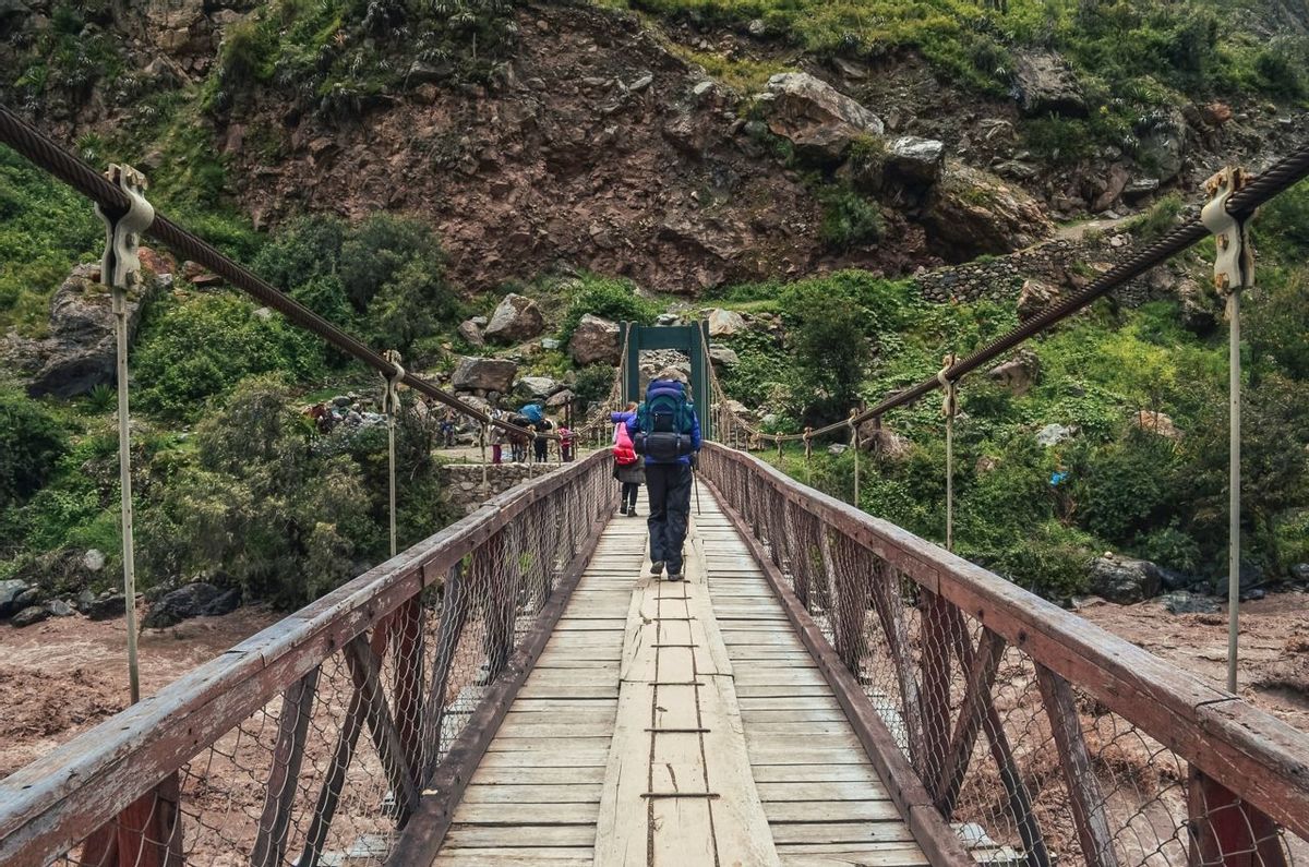 Male backpacker crossing the bridge over Vilcanota river to start inca trail to Machu Picchu archaeological site from the In…