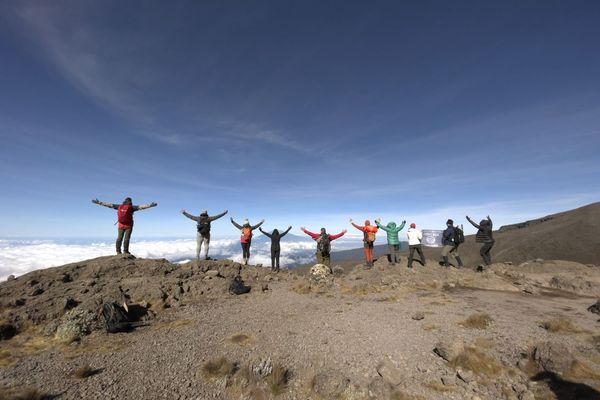 Hikers standing in a line over a wide vista holding their arms wide in celebration on the trek to Kilimanjaro