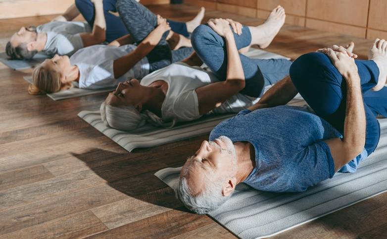 group of senior people stretching in yoga mats in studio