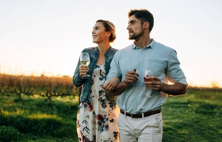 Man and woman with a drink walking outdoors. Couple together with a glass of wine in vineyard. Man and woman with a drink walking outdoors. Couple together with a glass of wine in vineyard.