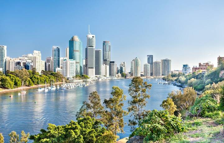 Blue water river surrounded by trees beside a modern cityscape including lots of tall buildings under blue sky called Brisb… Blue water river surrounded by trees beside a modern cityscape including lots of tall buildings under blue sky called Brisb…