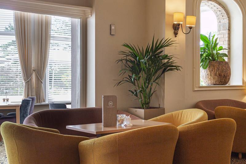 Hotel dining room at The Moorland Hotel in Dartmoor, yellow tub chairs surround a wooden square table.
