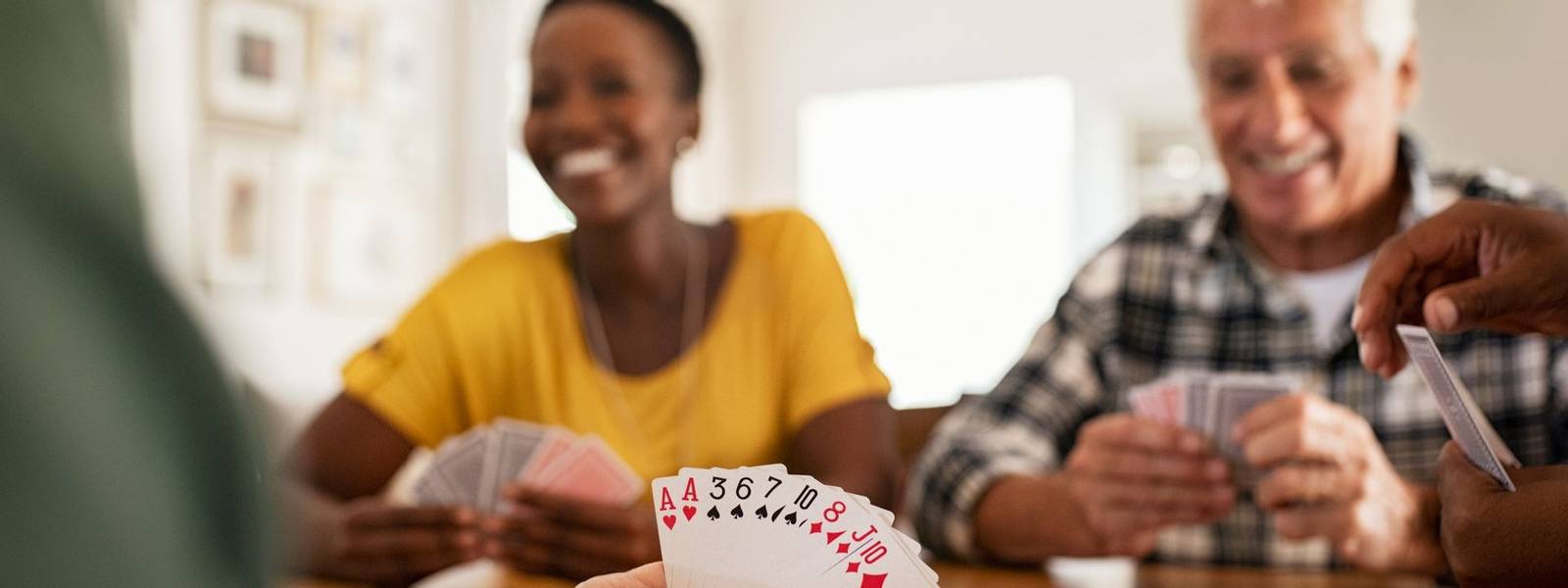Closeup of woman hand holding playing cards. Group of mature friends relaxing and playing cards together. Senior people and …