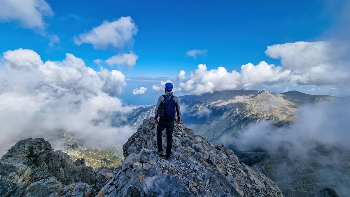 Rear view of man with climbing helmet on cloud covered mountain summit of Mytikas Mount Olympus, Mt Olympus National Park, M…