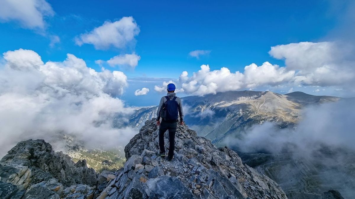 Rear view of man with climbing helmet on cloud covered mountain summit of Mytikas Mount Olympus, Mt Olympus National Park, M…