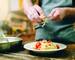 Male chef grates cheese in to the plate with fresh cooked pasta, pan on wooden kitchen table. Homemade fettuccine preparatio…