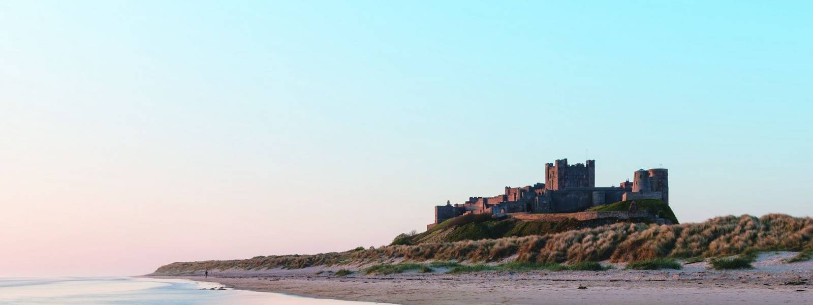 Beautiful landscape image of Bamburgh Castle on Northumberland coast at sunrise with vibrant colors