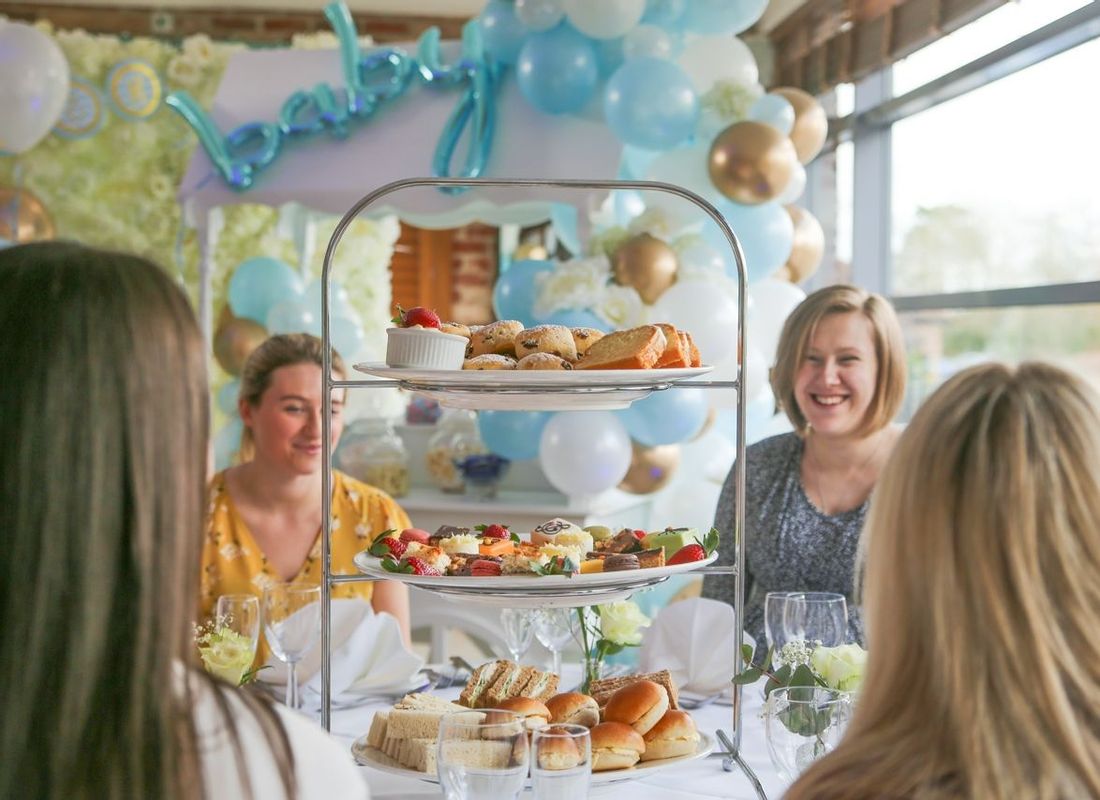 Group of friends celebrating a baby shower with large afternoon tea, sweet cart and balloons