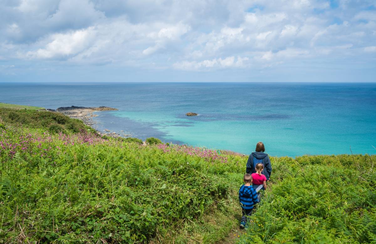 Family walking on a small path along the stunning Cornish coastline near St. Ives in Cornwall, England, UK