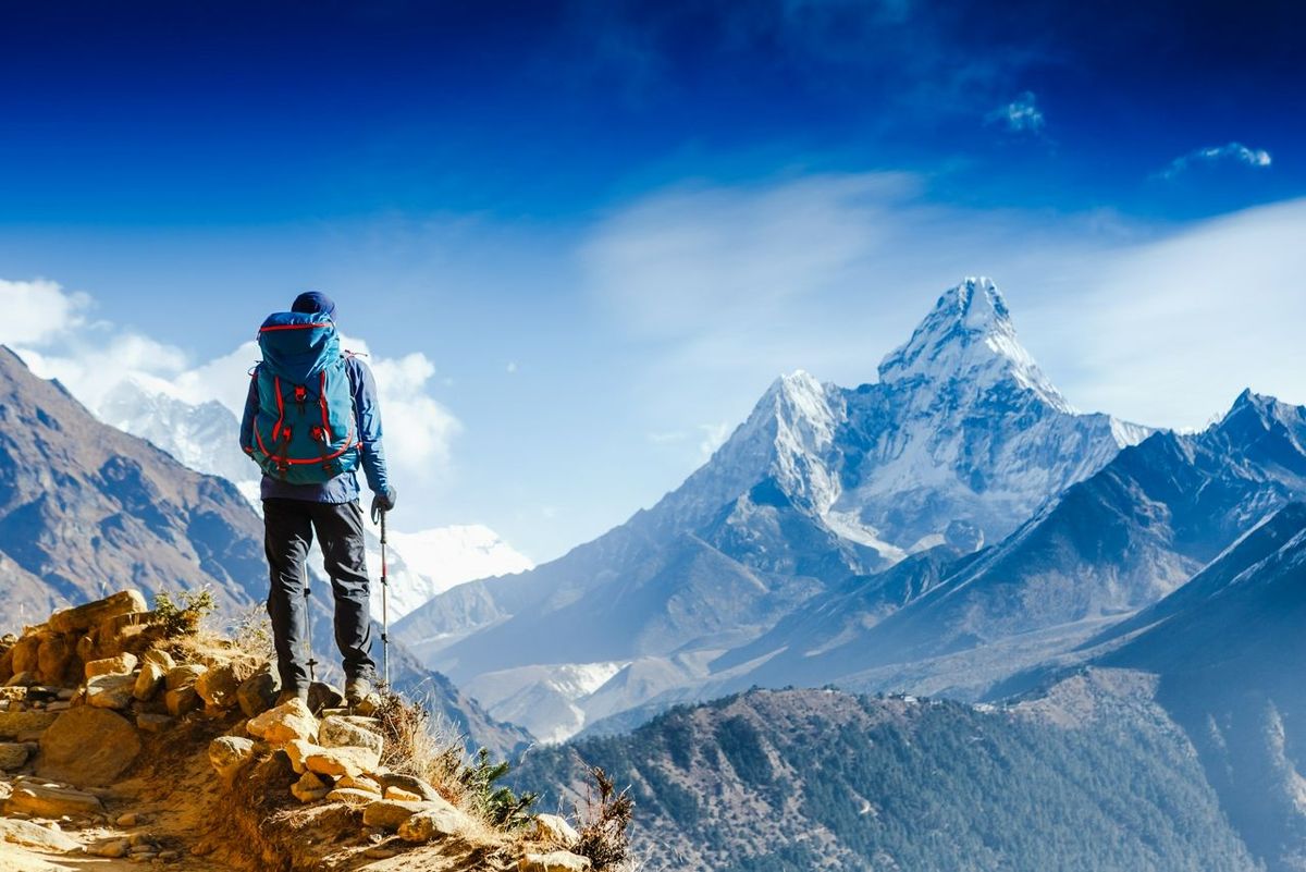 Hiker with trekking poles stands on the slope against the background of high snow-capped mountains