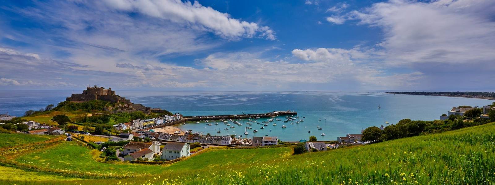 Image of Gorey Castle with Harbour, Grouville Bay calm sea and blue sky and clouds. Jersey, Channel Islands.