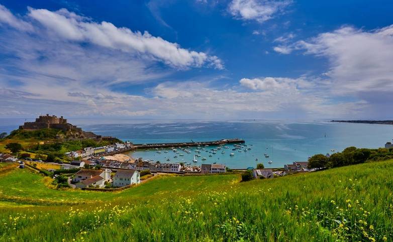 Image of Gorey Castle with Harbour, Grouville Bay calm sea and blue sky and clouds. Jersey, Channel Islands.